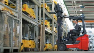 Staplerfahrer sitzt in Linde Gabelstapler und hebt Palette ins Regal