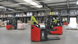Verschiedene Hochhubwagen und Gegengewichtsstapler von Linde MH fahren im Lager schnell aneinander vorbei
