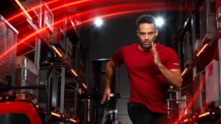 Ein Athlet läuft in einer Lagerhalle, im Hintergrund ist der Linde MH-Schubmaststapler Ri16 zu sehen.