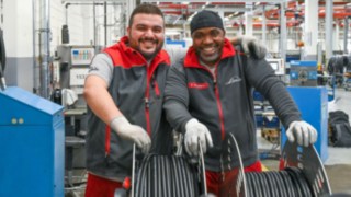 Zwei Mitarbeitende stehen in einer Fertigungshalle vor aufgewickelten Kabeln und Produktionsanlagen.
