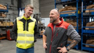 Zwei Mitarbeitende tauschen sich in einem Lagerbereich mit Regalsystemen aus.