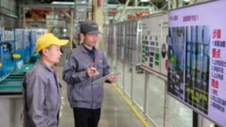 Mitarbeitende überwachen Produktionsprozesse an digitalen Anzeigetafeln in einer Fertigungshalle.