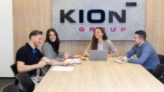 Besprechungsteam an einem Konferenztisch vor einem KION Group LOGO