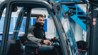Mitarbeitender bedient ein Flurförderfahrzeug in einer Produktions- oder Logistikumgebung.