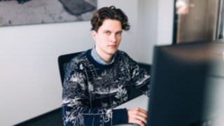 Ein junger KION Automation-Mitarbeiter sitzt konzentriert vor einem Monitor an einem modernen Arbeitsplatz im Büro. 