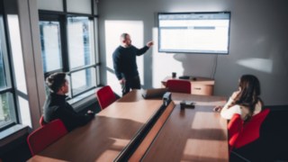 Drei Personen halten ein Teammeeting zu Intralogistik- und Automationsprojekten in einem Besprechungsraum mit einer Präsentation auf dem Bildschirm.