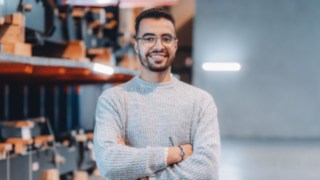 Ein junger Kollege mit Brille und Uhr steht selbstbewusst mit verschränkten Armen im Lager und ist engagiert in der Inbetriebnahme bei Linde. 