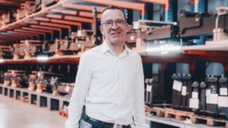 Ein Projektmanager in heller Business-Kleidung befindet sich in einer technischen Lagerumgebung, die das Arbeitsumfeld bei Linde im Bereich Automatisierungsprojekte darstellt. 