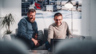 Zwei Mitarbeitende sitzen entspannt auf einem Sofa und lachen gemeinsam über Inhalte auf einem Laptop, was ein inspirierendes Arbeitsumfeld symbolisiert, das Raum für Kreativität, Innovation und persönliche Weiterentwicklung bietet.