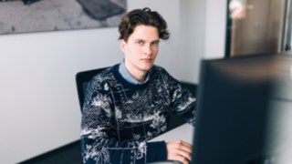 Ein junger KION Automation-Mitarbeiter sitzt konzentriert vor einem Monitor an einem modernen Arbeitsplatz im Büro. 