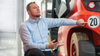 Person steht vor Gabelstapler und zeigt auf ein Schild 